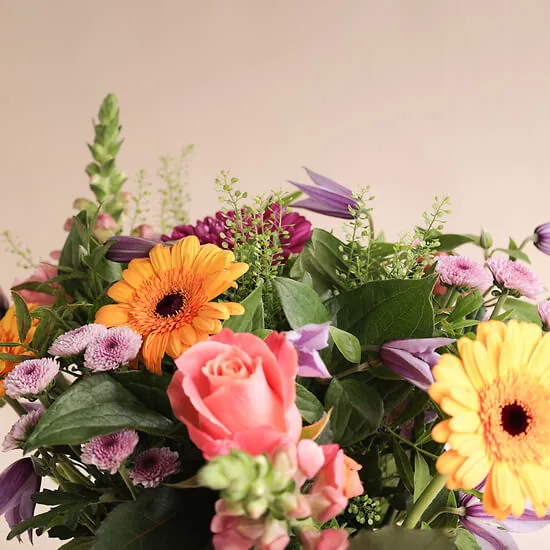 Close-up of orange gerberas, a pink rose and purple clematis in the Poésie de saison bouquet